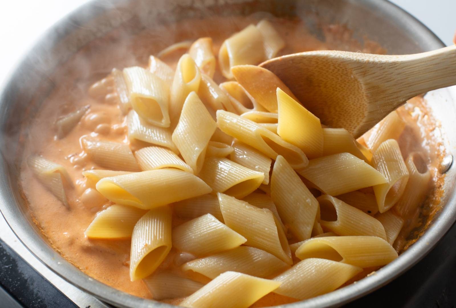 Mixing pasta into red pepper sauce.