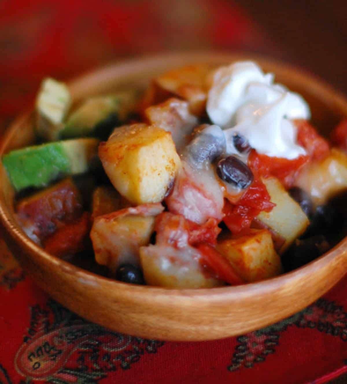 Cheesy roasted potato nachos in a wooden dish with toppings.