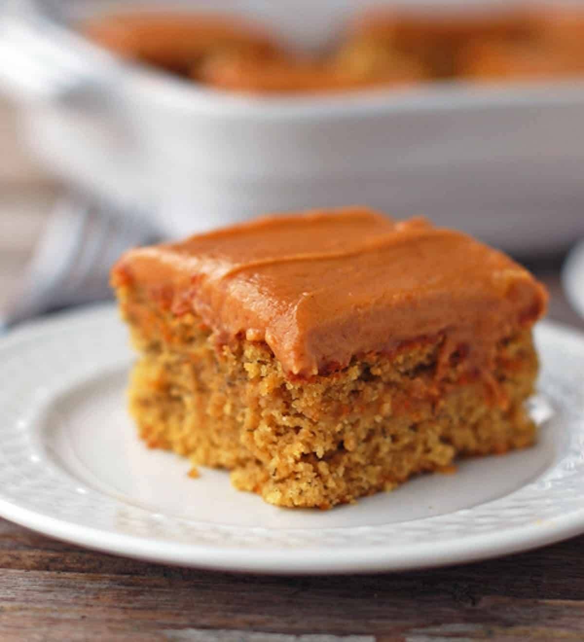 One piece of banana cake with peanut butter frosting on a white plate.