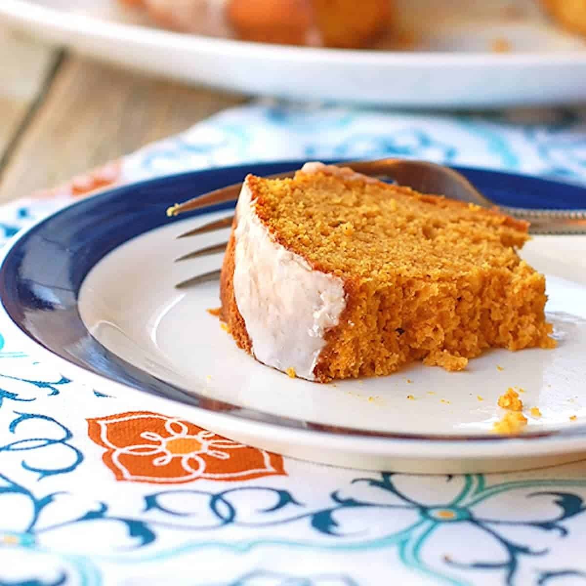 Pumpkin bundt cake with cinnamon glaze on white plate on a colorful napkin.